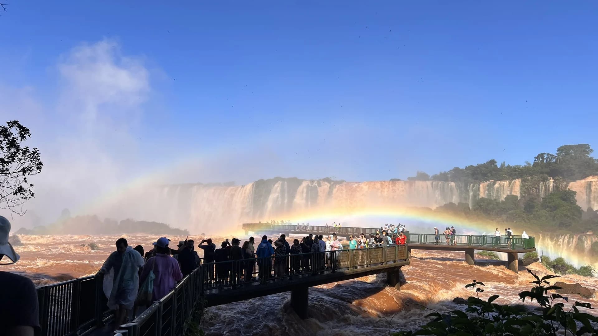 Turistas na passarela das Cataratas do Iguaçu com arco-íris duplo sobre a Garganta do Diabo