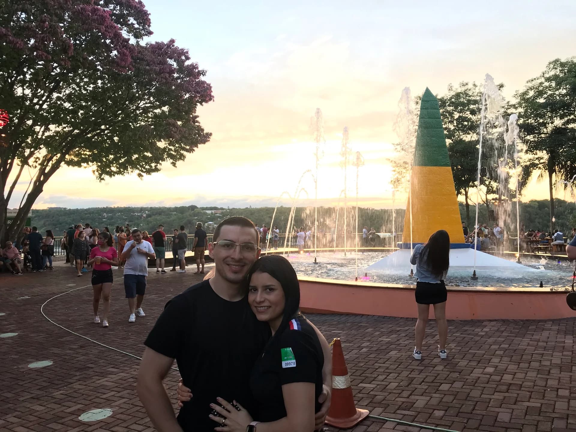Casal abraçado no Marco das Três Fronteiras com fontes ao pôr do sol
